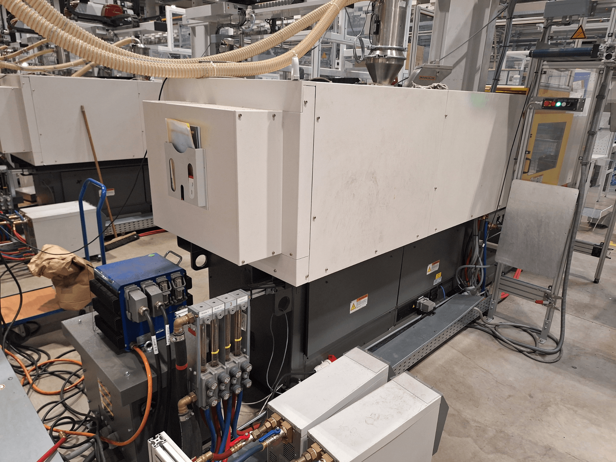 Fabrika ortamında endüstriyel ekipman; kontrol paneli, hortumları ve elektrik bağlantıları olan büyük bir makine, yandan görünüm.