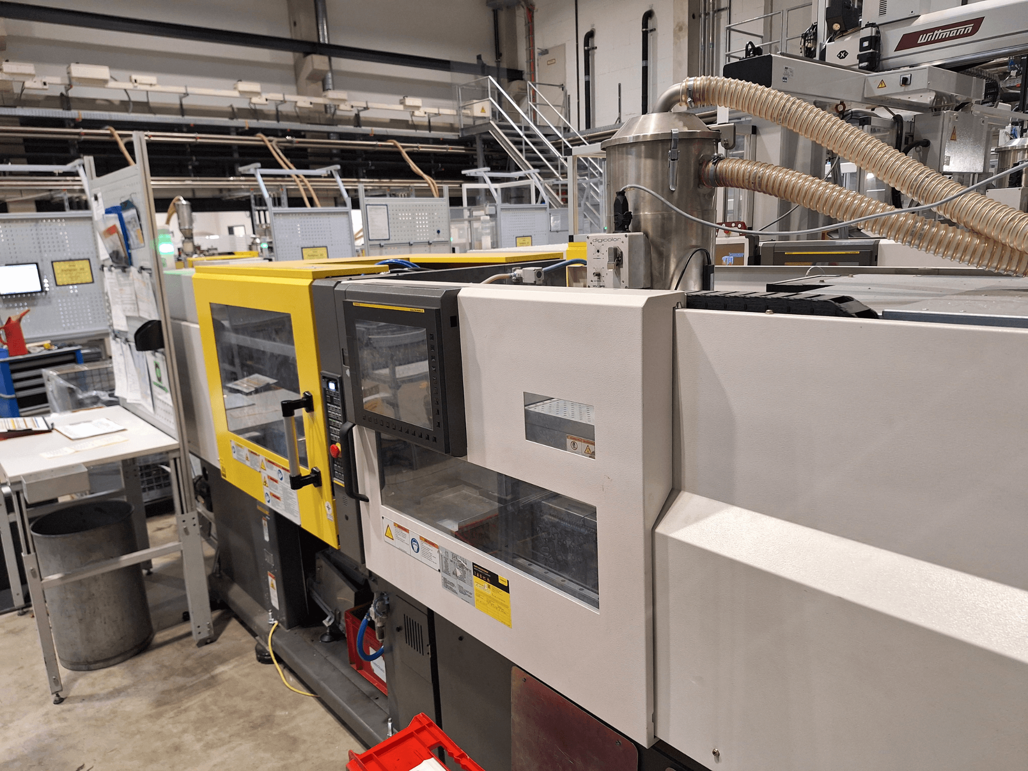 Kontrol paneli ve egzoz sistemi ile sarı ve gri bölümleri olan çok renkli bir enjeksiyon kalıplama makinesinin önden görünümü.