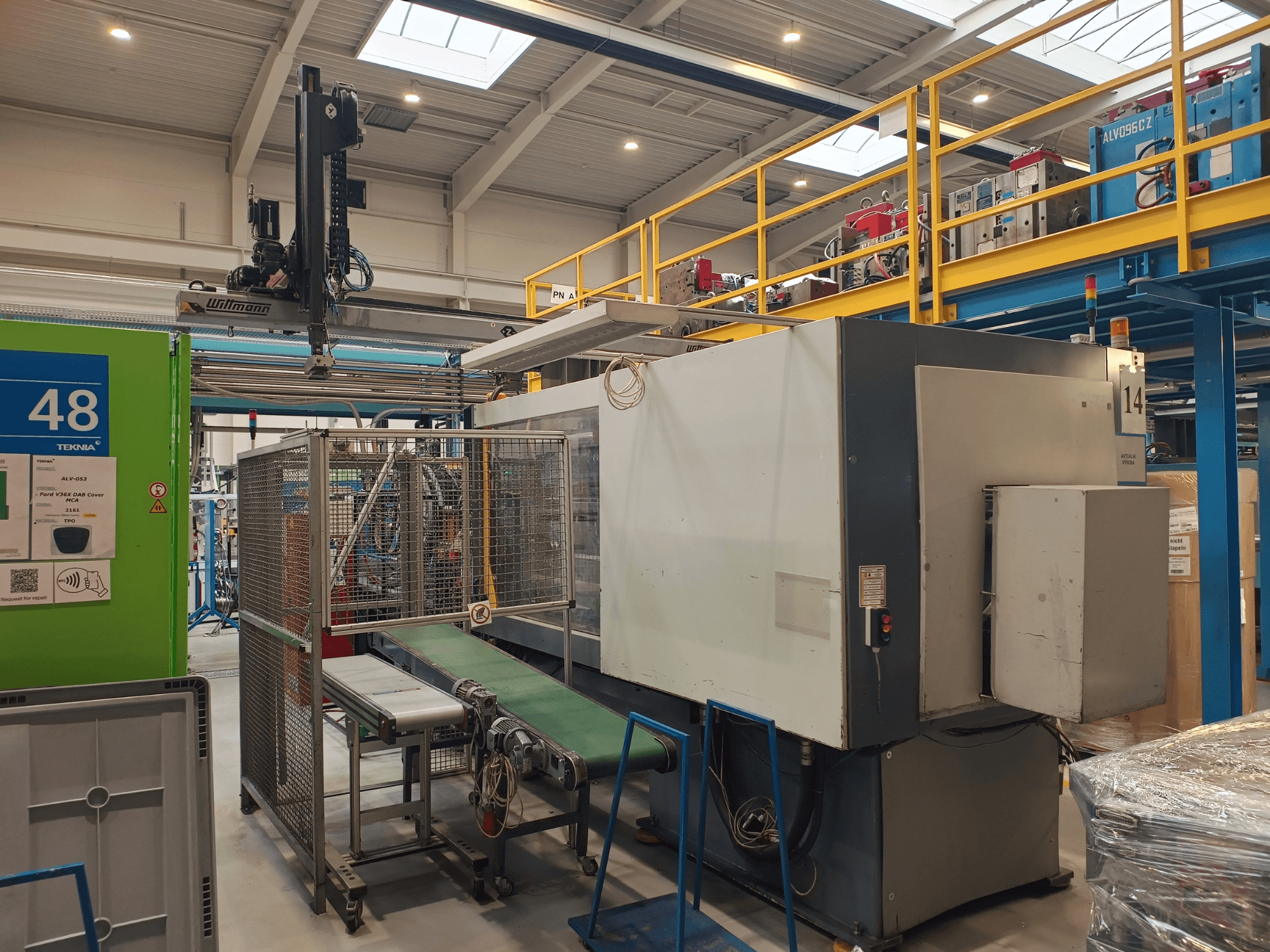 '48' etiketli yeşil konveyör ve tavan vinci ile endüstriyel otomasyon ekipmanı; makinenin fabrika zemininde yandan görünümü.