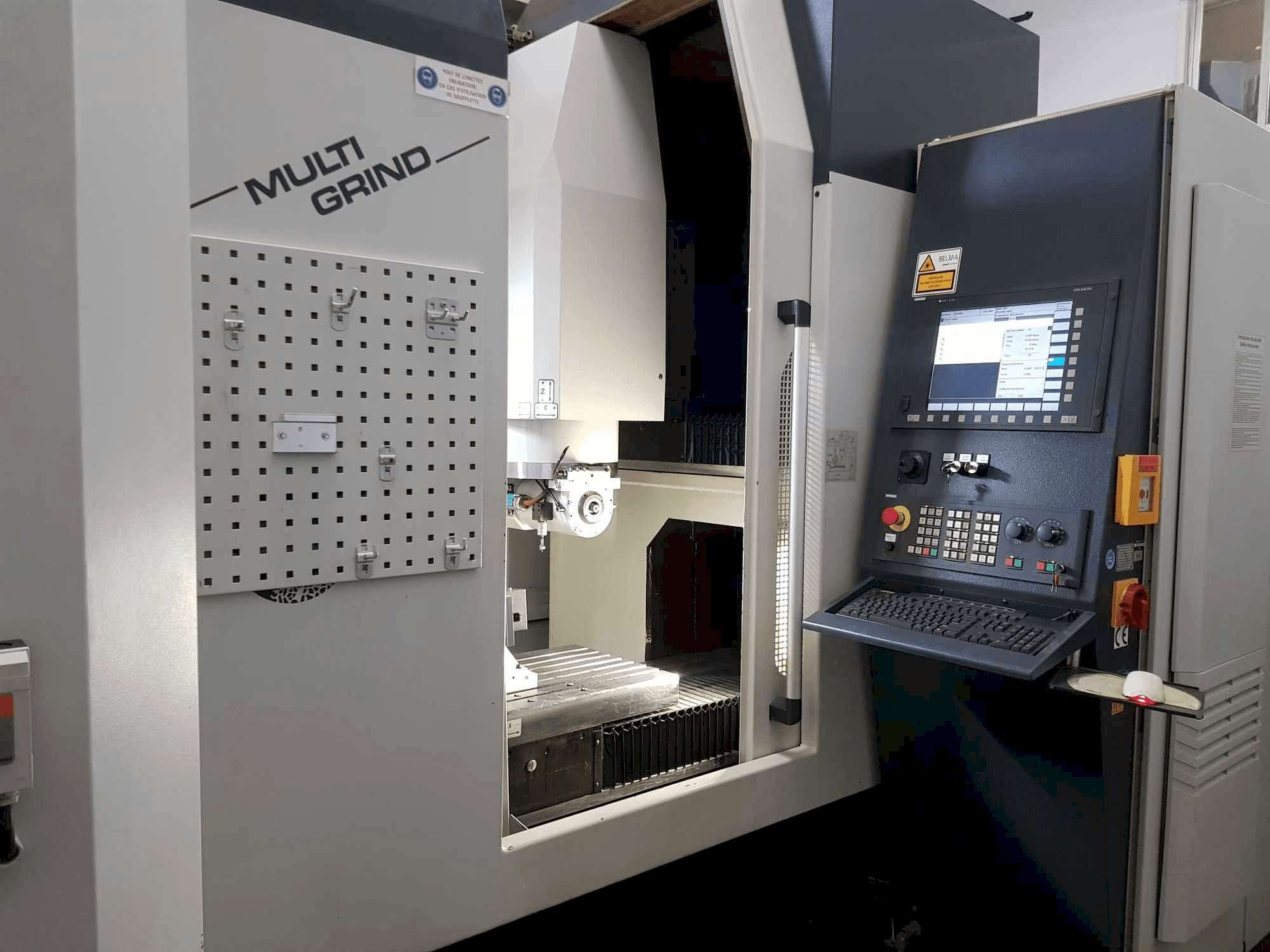 Önden görünümlü Multi Grind CNC makinesi, bir kontrol paneli, depolama panosu ve açık bir çalışma alanı içerir.